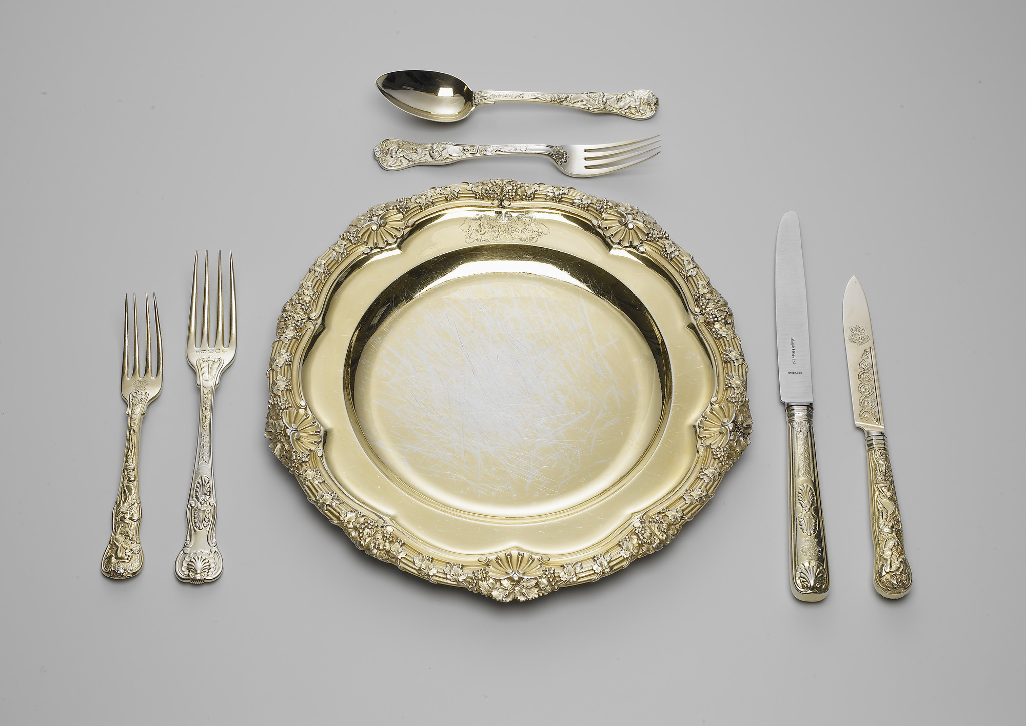 A set of silver-gilt plates; the reeded rim cast with fruiting vines and scallop shells. The plate is engraved with the Royal coat of arms, with supporters, mantling and coronet.